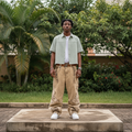 Nigerian male model full body wearing men's sage green pinstripe boxy short-sleeve shirt open over white tee
