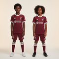 Black Nigerian boy and girl wearing Liverpool FC kids dark burgundy football kit with white Adidas stripes
