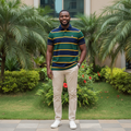 Nigerian male model wearing men's striped polo shirt in navy, green and gold, garden setting