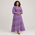 Black Nigerian model wearing a lavender tiered pleated gown with bell sleeves and metallic floral-pattern panels