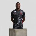 Nigerian male model wearing black galaxy splatter graphic football jersey on concrete plinth