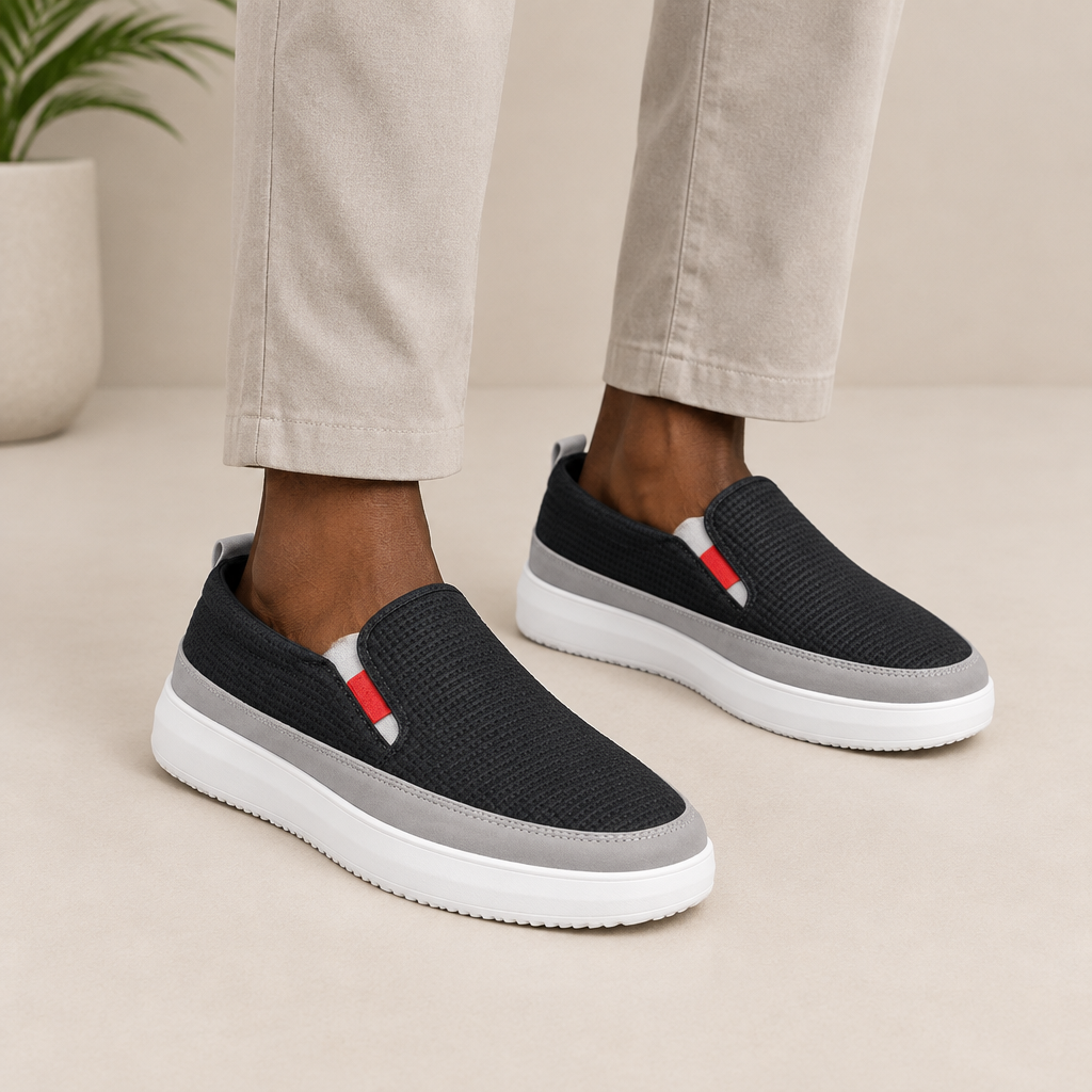 Black textured slip-on shoes with grey trim and white platform soles worn on both feet