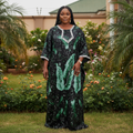 Nigerian woman wearing deep green sequin bubu dress with white embroidered neckline in garden setting