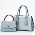 Pale blue textured twin-handle handbag beside smaller blue flap bag with brown handle