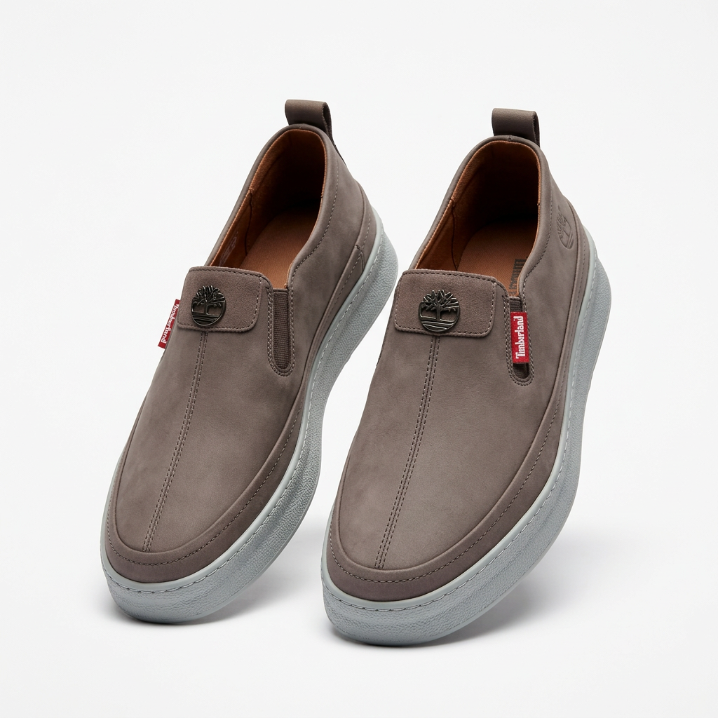 Pair of grey-taupe stitched slip-on shoes with metal crests and pale grey soles on white