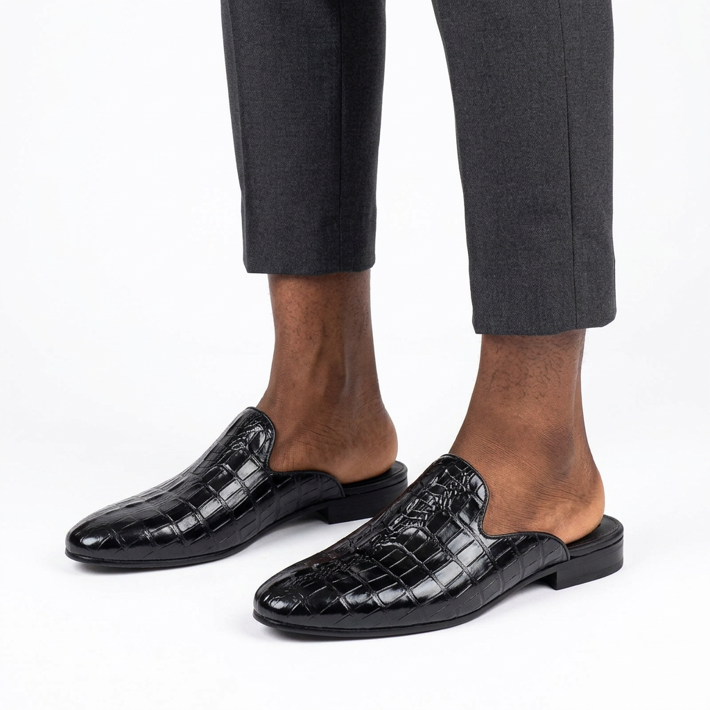 Pair of black crocodile-effect mule shoes properly worn on both feet with tailored trousers