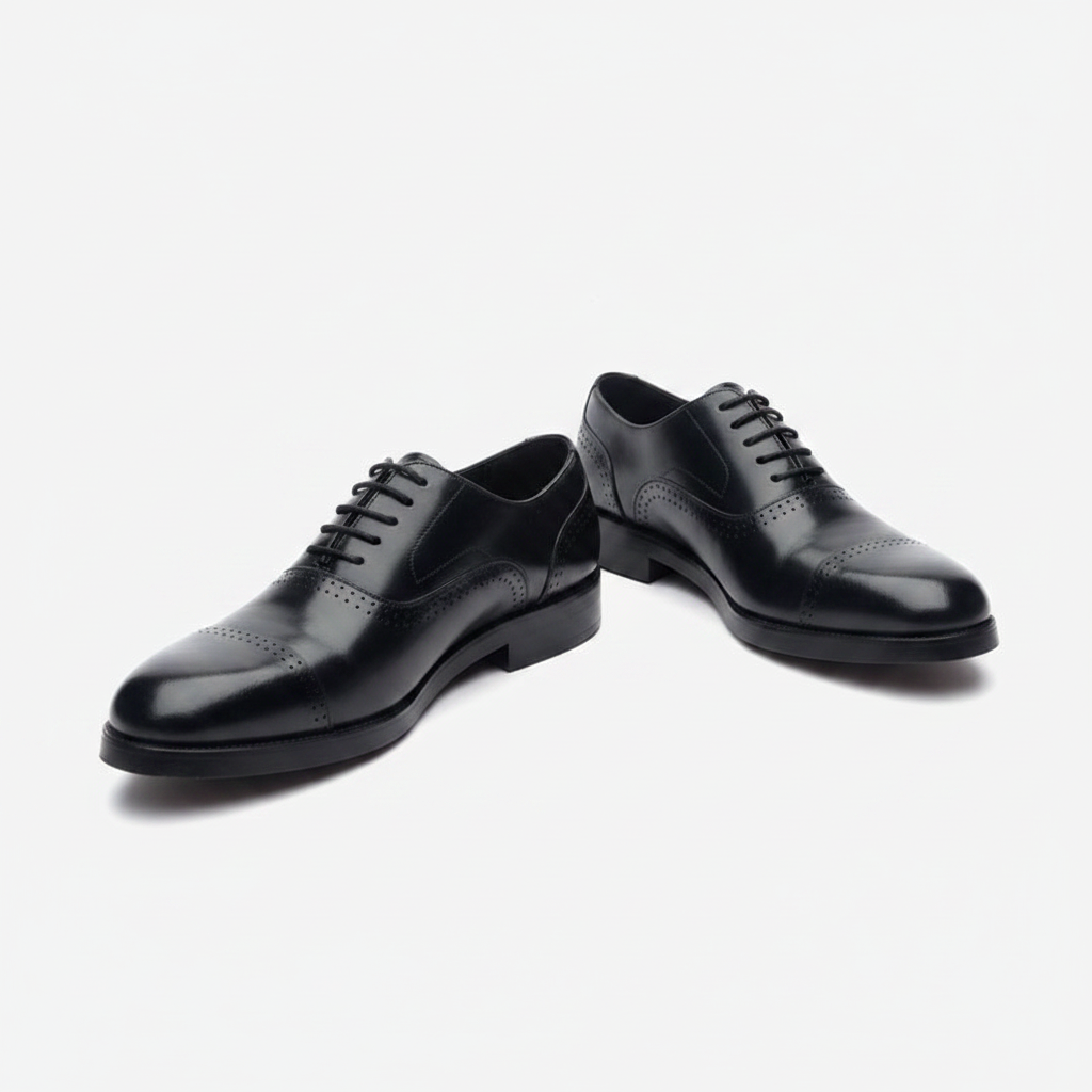 Polished black leather cap-toe derby shoes, centred on a plain off-white background