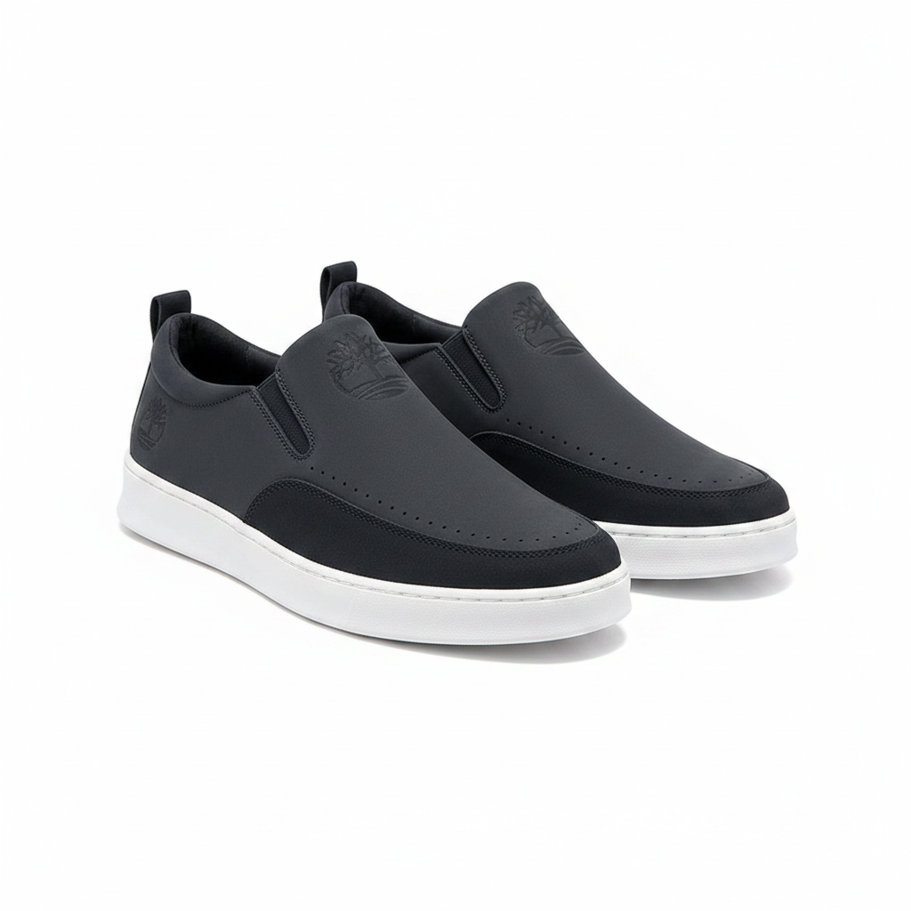 Men's dark navy charcoal nubuck slip-on sneakers with moccasin toe, perforated detailing and white rubber cupsole, ghost mannequin pair view on white background