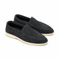 A pair of charcoal-black suede moc-stitch loafers with cream soles on white