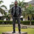 Nigerian male model wearing matte black faux leather biker jacket — full body street style
