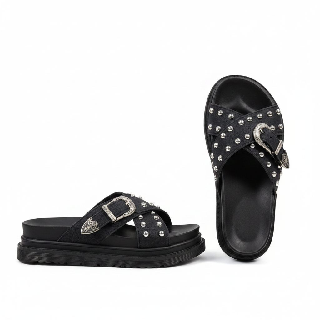 Pair of black cross-strap platform slide sandals with silver studs and western buckle on white background