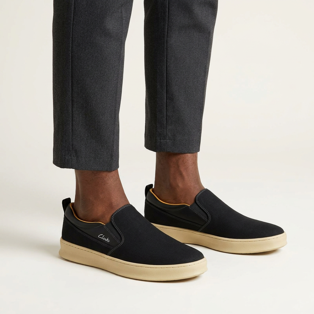 Both feet wearing black slip-on shoes with cream soles against a plain off-white background