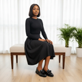 Nigerian female model seated in black midi skirt wearing black croc-embossed patent loafers with bow detail
