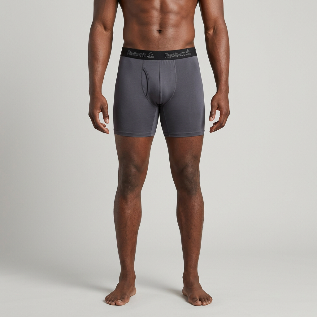 Male model wearing charcoal boxer briefs alone on a plain studio background