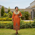 Nigerian female model wearing burnt orange peacock print puff sleeve midi gown in garden setting