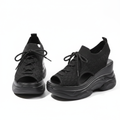 Pair of all-black peep-toe knit wedge sneakers with lace-up detail and chunky wedge sole on white background