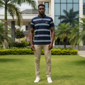 Nigerian male model wearing men's navy all-over stripe polo shirt with white and green stripes, garden setting