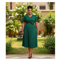 Nigerian female model wearing forest green pleated midi gown with rose corsage in upscale garden setting