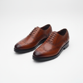 Tan burnished leather wingtip brogue oxfords, centred on a plain off-white background