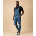 Man wearing mid-blue denim bib overalls with ripped knees over a black t-shirt