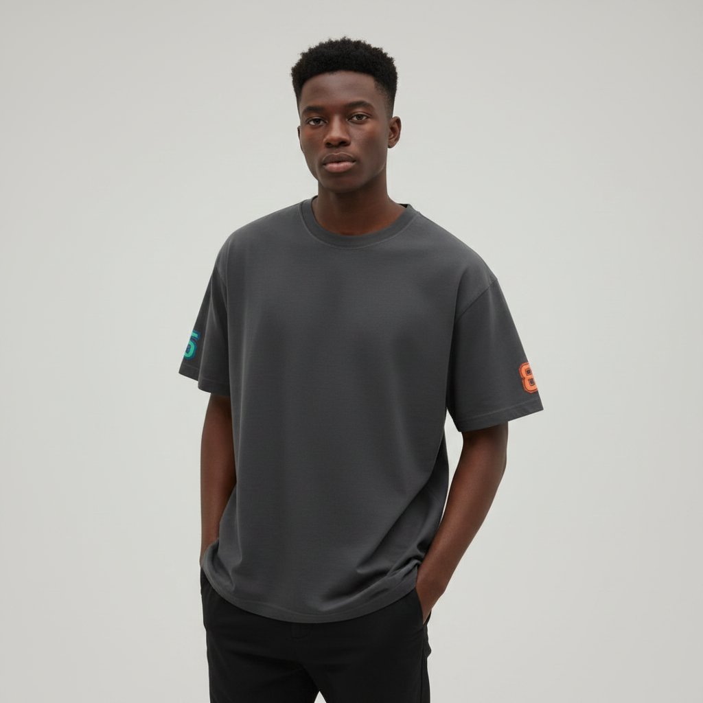 Young Nigerian male wearing dark charcoal oversized plain crew neck tee with teal sleeve logo