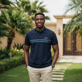 Nigerian male model wearing men's navy polo shirt with white and green chest stripe, garden setting